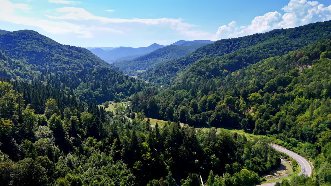 Serene mountain valley with winding road. Lush green mountains surround a scenic valley with a winding road under a clear blue sky, showcasing nature's beauty