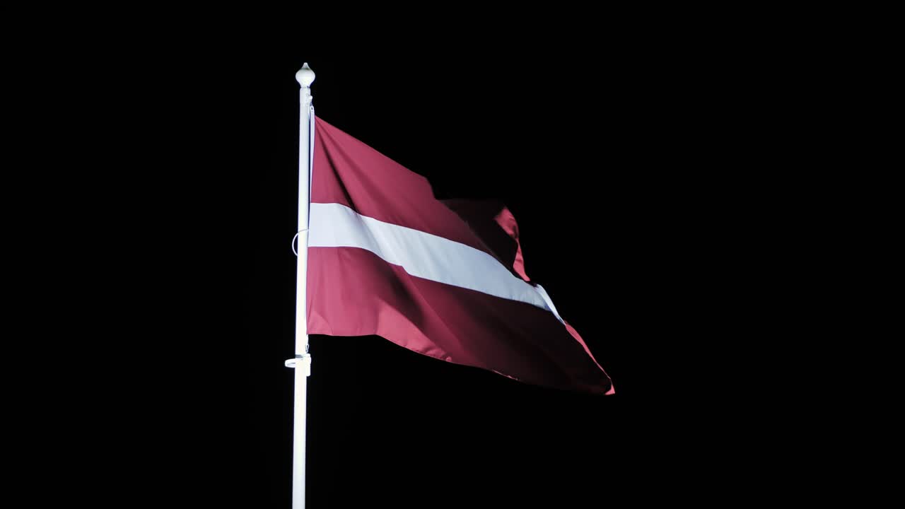 Symbolic red and white flag of Latvia moving against dark sky in crisp wind