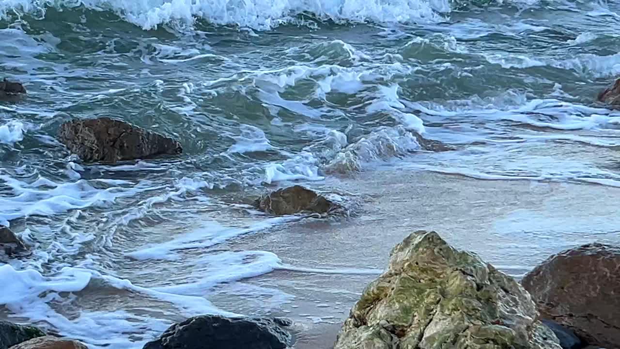 Onde e spuma che si infrangono tra le rocce su una spiaggia sabbiosa