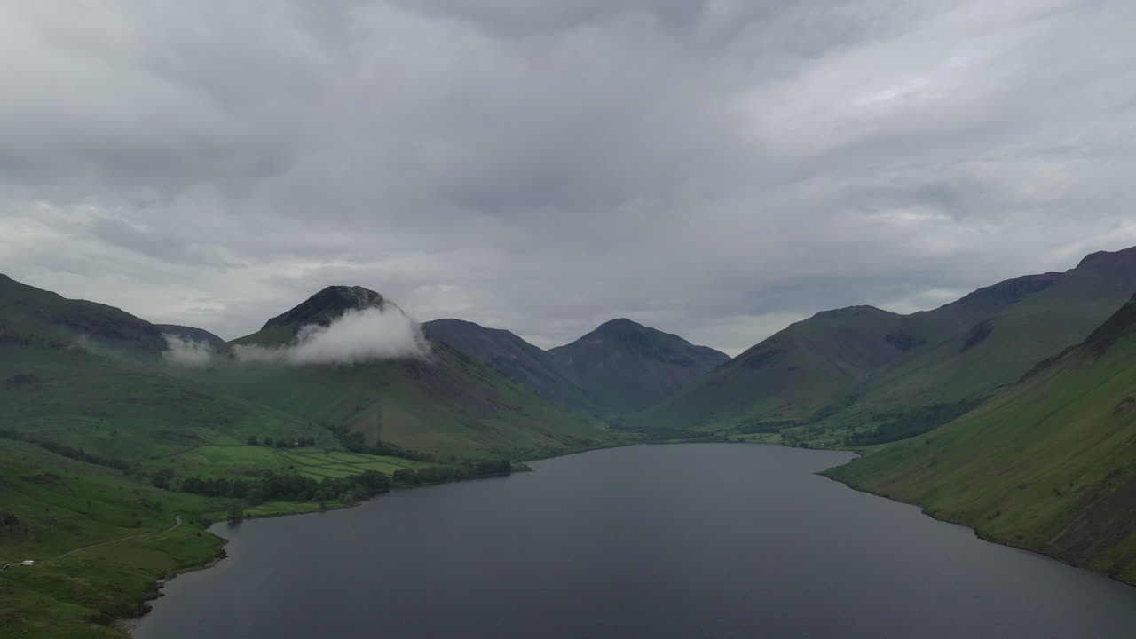toma aérea de un lago rodeado de montañas con nubes bajas, día de verano gris