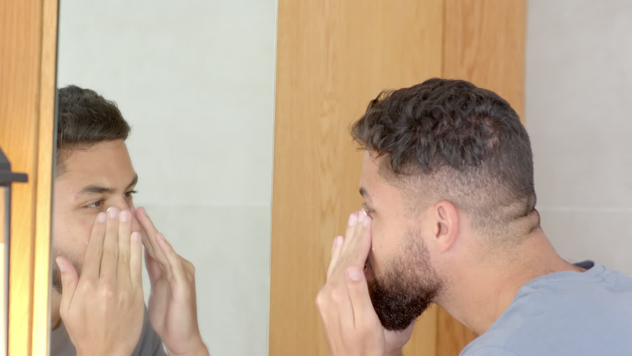 Grooming beard, man looking in bathroom mirror, focusing on appearance