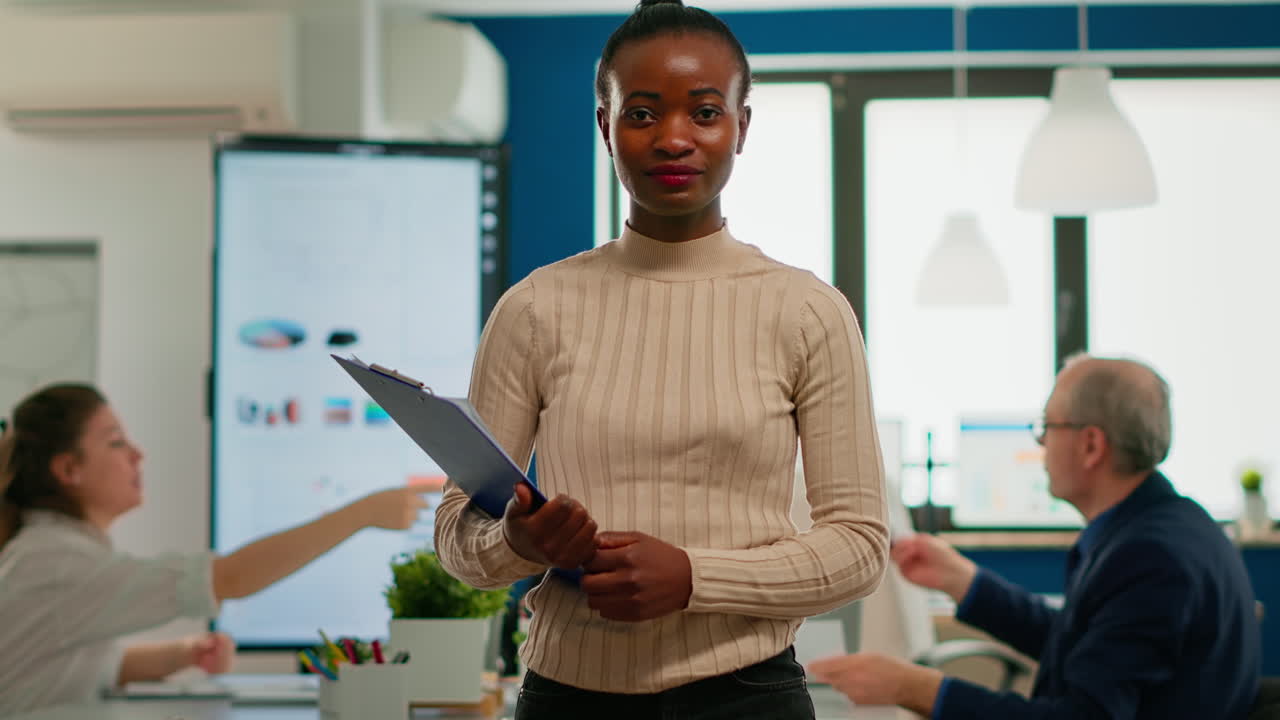 African woman manager looking at camera smiling, holding clipboard