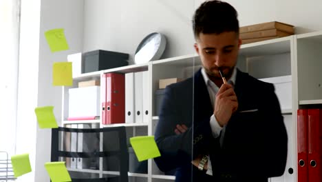young businessman making notes in documents standing near glass wall