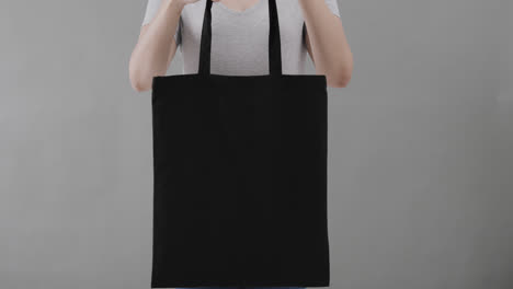 caucasian woman wearing white t-shirt holding black bag on grey background, copy space, slow motion