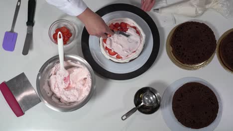 chef placing sliced strawberries on layer of cake that already has some cream on top.