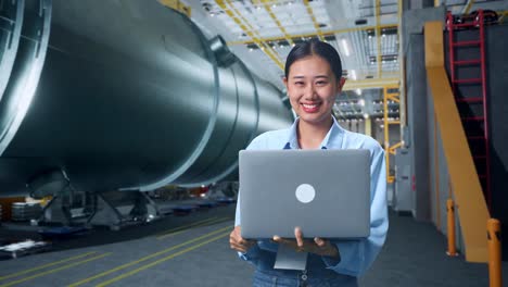 an asian business woman using laptop computer and smiling to camera in pipe manufacturing factory