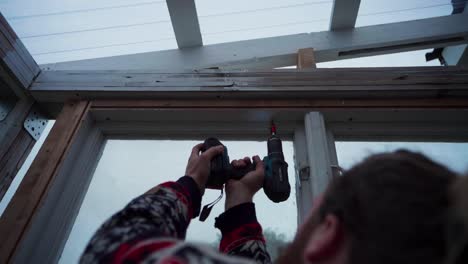 A-Man-is-Using-a-Drill-to-Drive-a-Nail-into-Wood---Building-a-Greenhouse-in-Indre-Fosen,-Norway---Close-Up