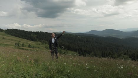 Groom,-brunette-young-man-stay-on-the-top-of-the-mountains.-Raises-his-hand-up