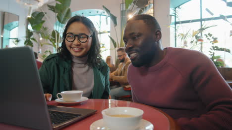 Asian-Woman-and-African-American-Man-Working-on-Laptop-and-Talking-in-Cafe