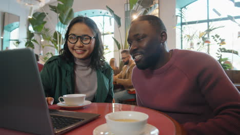 asian woman and african american man working on laptop and talking in cafe