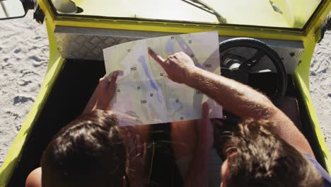 pareja caucásica de pie cerca de la playa buggy por el mar leyendo un mapa