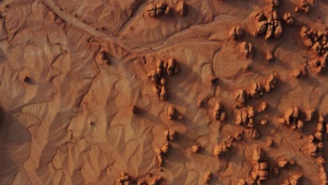 Stunning-top-bird's-eye-aerial-drone-view-of-the-beautiful-Goblin-Valley-Utah-State-Park-with-small-strange-mushroom-rock-formations,-dried-sand,-a-dried-river-bed,-and-red-rock-butte's-below