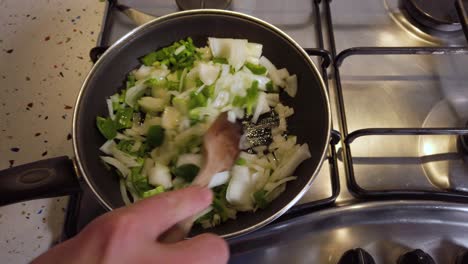 mano revuelve pimiento verde y cebolla en una sartén pequeña, cierre lento