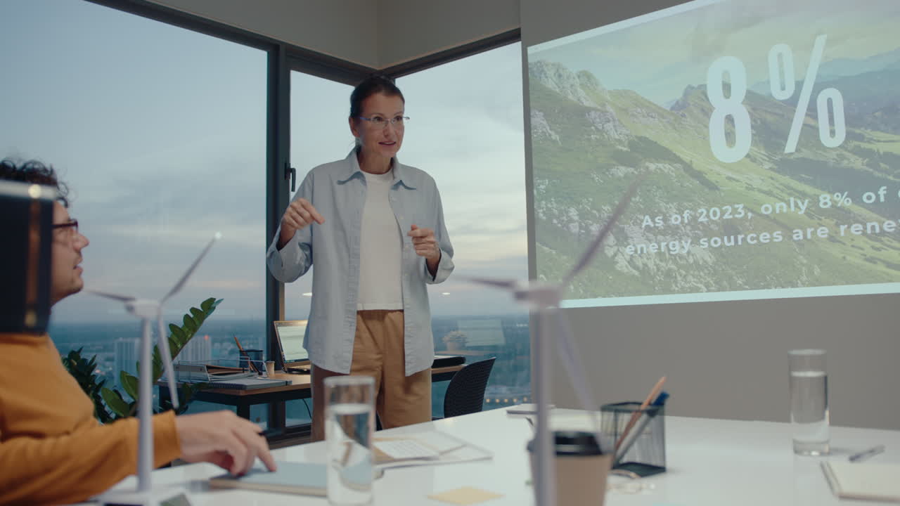 Female team leader explaining presentation on projection screen to colleagues during business meeting in green energy company in modern office with panoramic windows overlooking the cityscape