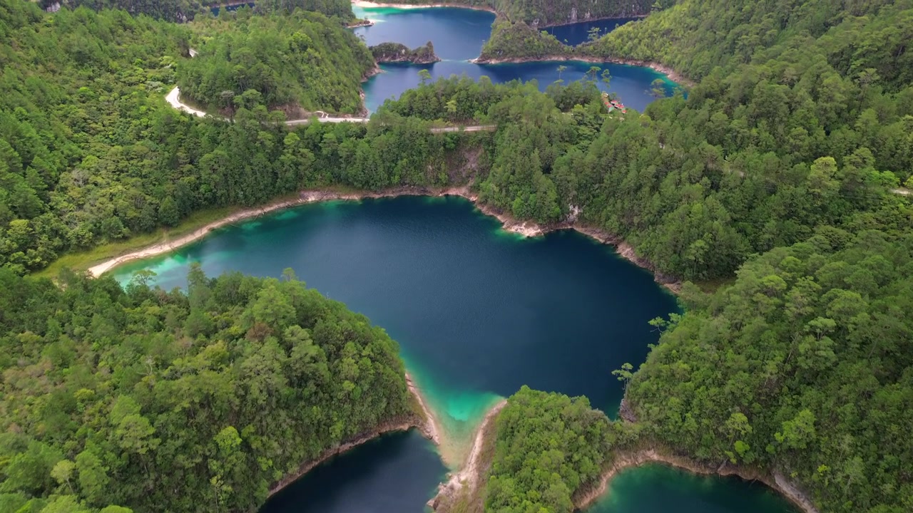 Långsam drönarvy framåt från luften som avslöjar en djupblå kratersjö med turkos strandlinje omgiven av tallskog i Montebello, Chiapas, Mexiko.