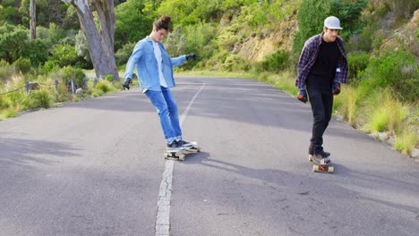 Front-view-of-cool-young-caucasian-skateboarders-skating-on-downhill-at-countryside-road-4k