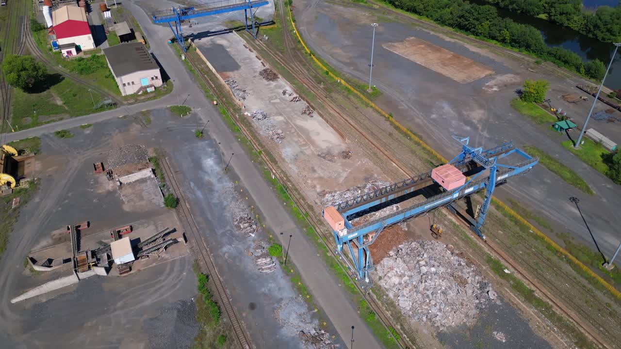 Gantry crane transporting scrap metal at Hennigsdorf electric steel mills on a sunny summer day. Tremendous aerial view flight drone shot from above