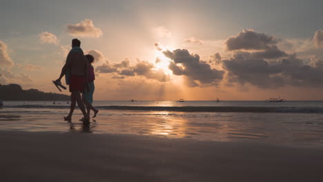 Pareja-De-Luna-De-Miel-Caminando-Sobre-Arena-Mojada-Junto-Al-Mar-Al-Atardecer-En-La-Playa-De-Jimbaran,-Bali,-Indonesia---Cámara-Lenta,-ángulo-Bajo