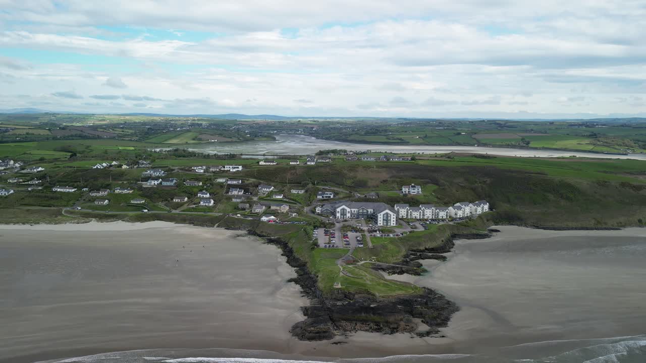 volando hacia atrás y revelando el panorama sobre la playa de inchidoney con acantilados, colina y pueblo en west cork, irlanda
