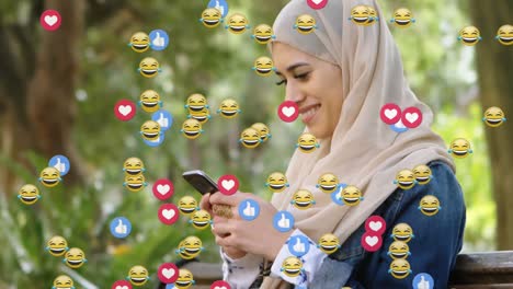 animation of od falling emojis over woman in hijab using smartphone