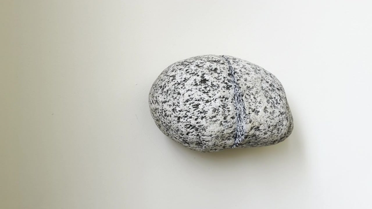 A stone hangs on a light beige wall, with little black spots, Zoom in shot