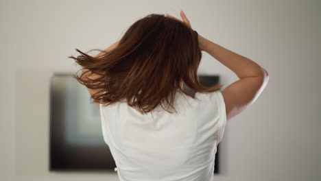 woman touches shaggy hair at running. sporty lady exercises through jog stroking hair in domestic gym. importance of physical activity for overall health