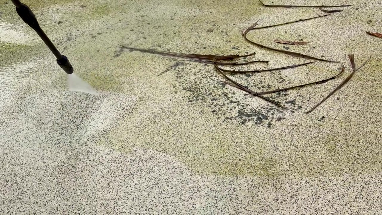 Nærbillede i slowmotion af en højtryksrenser, der fjerner grønne alger og snavs fra beton.