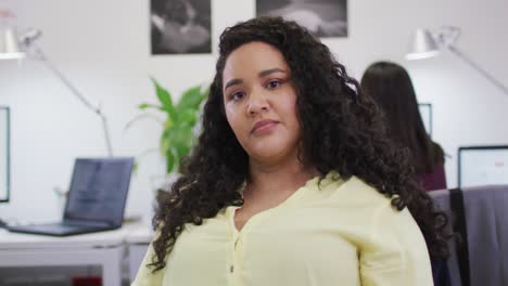 retrato de una mujer de negocios biracial sonriente mirando a la cámara en una oficina moderna