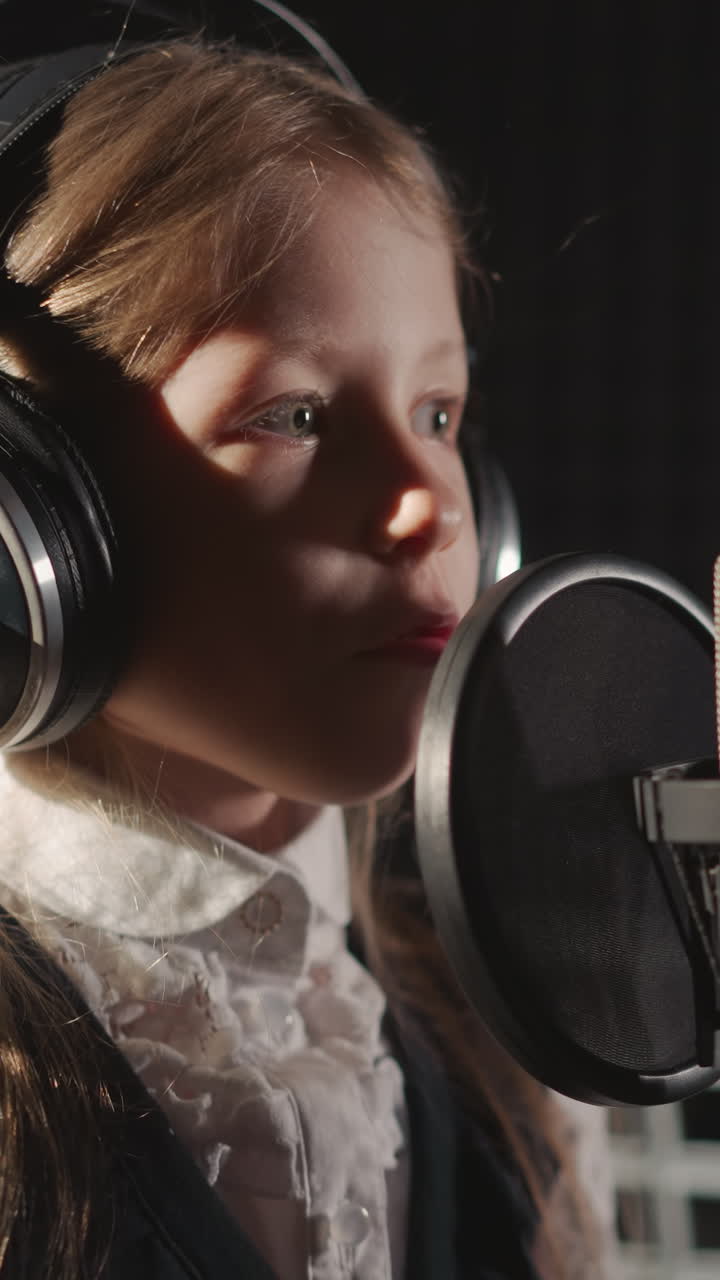 Girl in headphones sings in recording studio. surrounded by soundproof walls. Child demonstrates talent in front of microphone equipped with sound filter