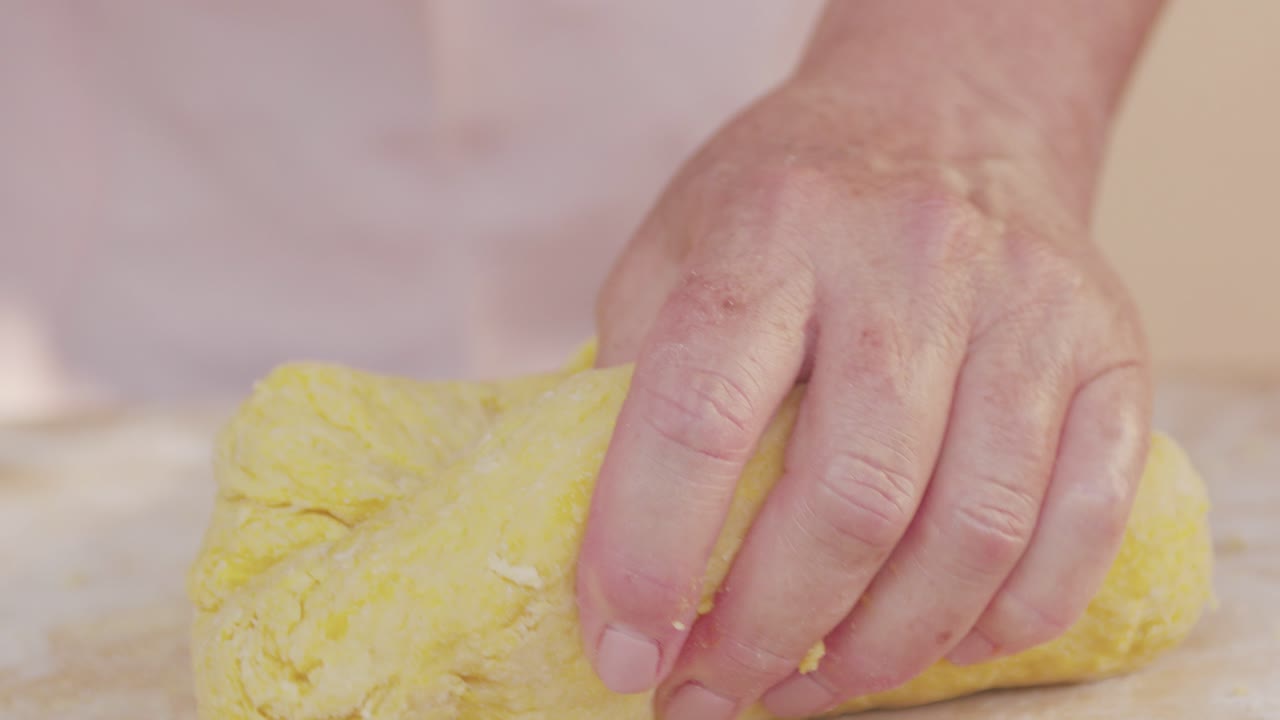 Close-up slow-motion of a hand kneading fresh egg pasta dough, showcasing traditional homemade Emilia-Romagna pasta making in a rustic kitchen setting. Authentic Italian cuisine