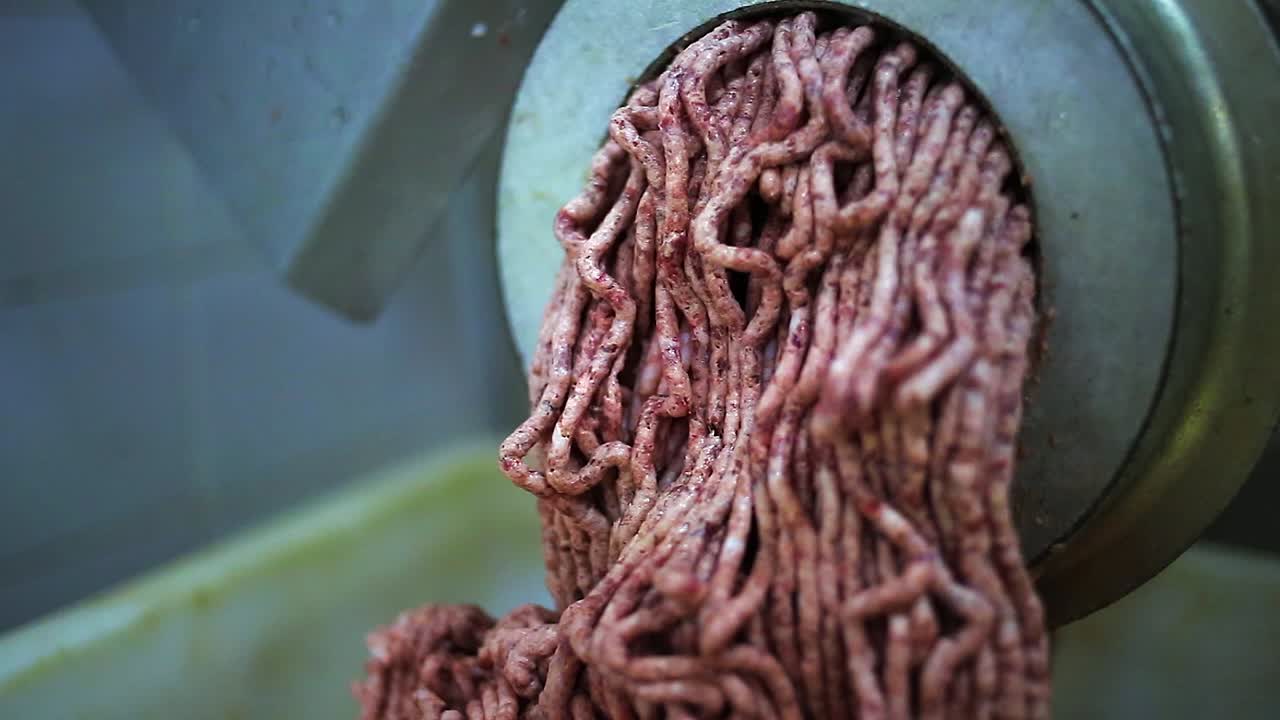 Fettiges rotes Fleisch kommt aus dem Fleischwolf in einer Metzgerei, Nahaufnahme