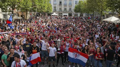 a celebratory crowd enthusiastically cheers with flags and a trophy, capturing the spirit of triumph and unity in a vibrant public square