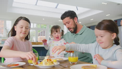 Familie-Mit-Down-Syndrom-Tochter-Sitzt-Zu-Hause-Am-Tisch-Und-Frühstückt