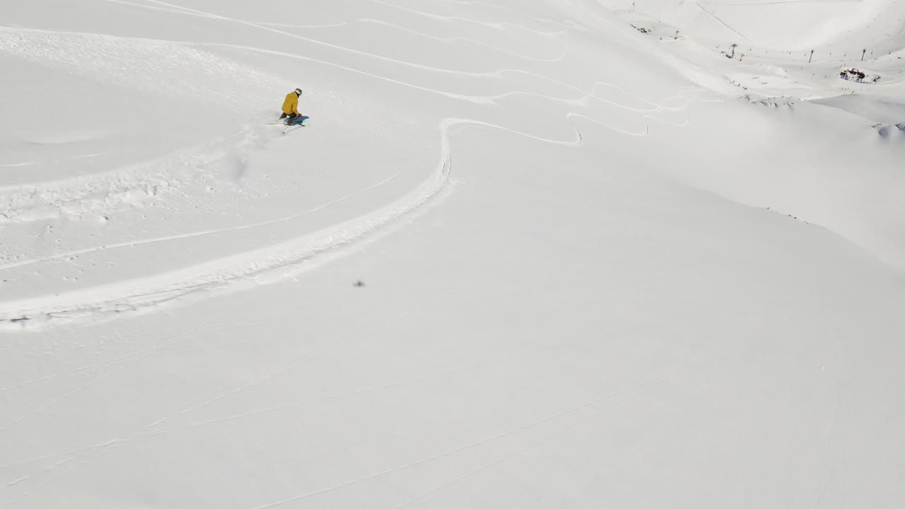 An exhilarating FPV drone shot capturing a skier carving through deep powder snow on a bright winter day. The dynamic perspective highlights the skier's movement and the untouched snowy terrain.