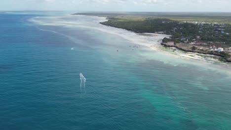 playa de kusini en el este de la isla de zanzíbar, tanzania áfrica, con un barco que avanza sobre los arrecifes de coral, tiro aéreo