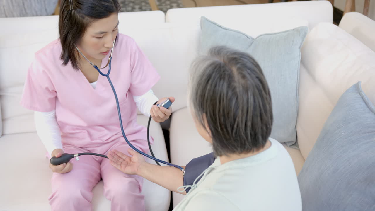 Nurse in pink scrubs checking blood pressure of senior patient at home