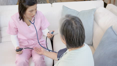 nurse in pink scrubs checking blood pressure of senior patient at home