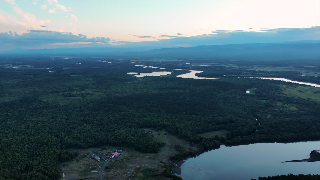 Aerial view of a river winding through a vast forest landscape with mountains in the background