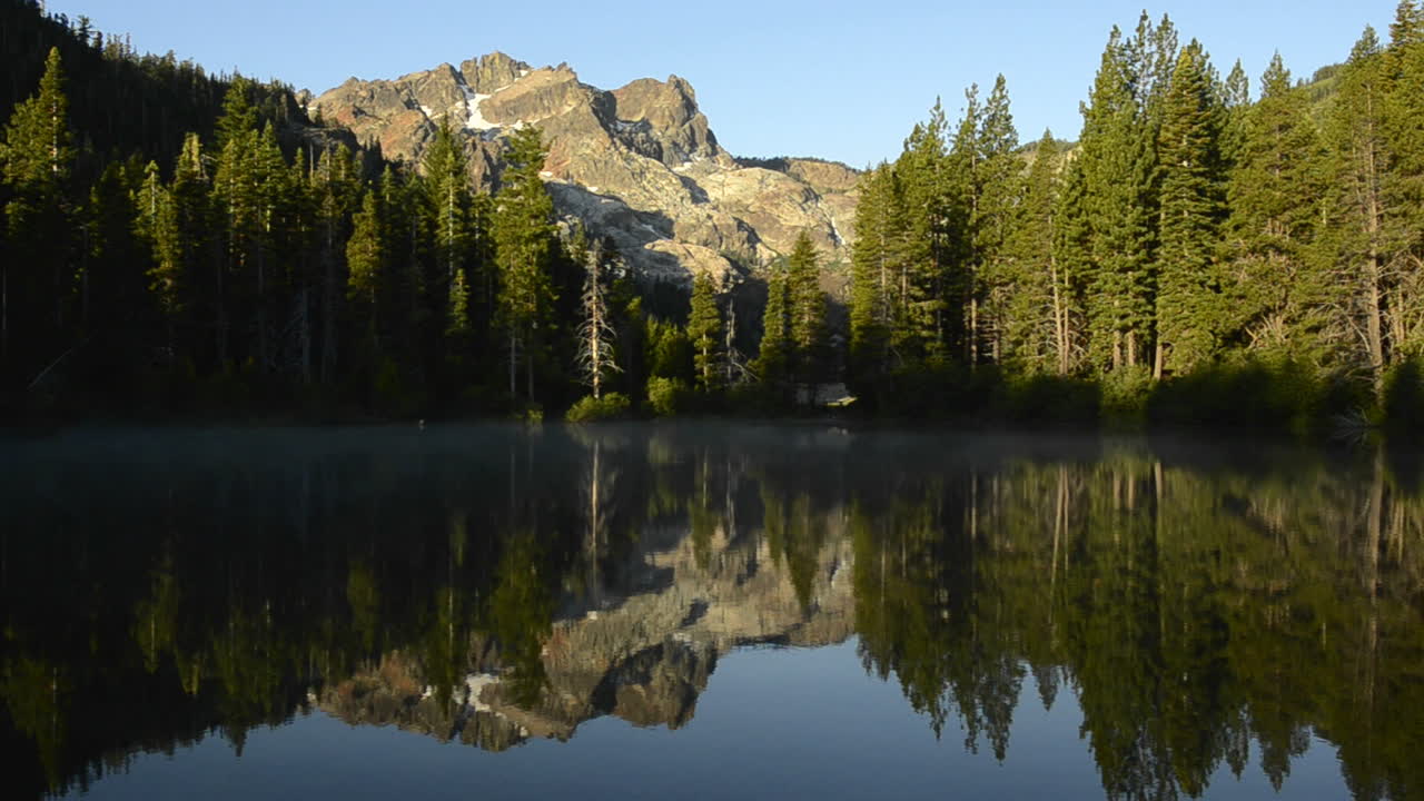 En morgenrefleksjon av Sierra Buttes på Sand Pond i Tahoe National Forest, California
