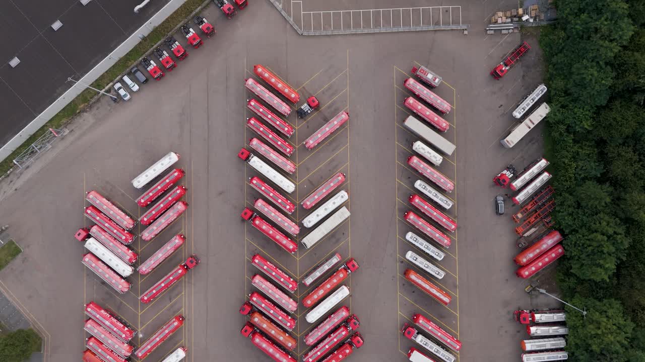 Overhead drone view of a logistics truck yard with parked red trucks in geometric rows, representing transport and industry