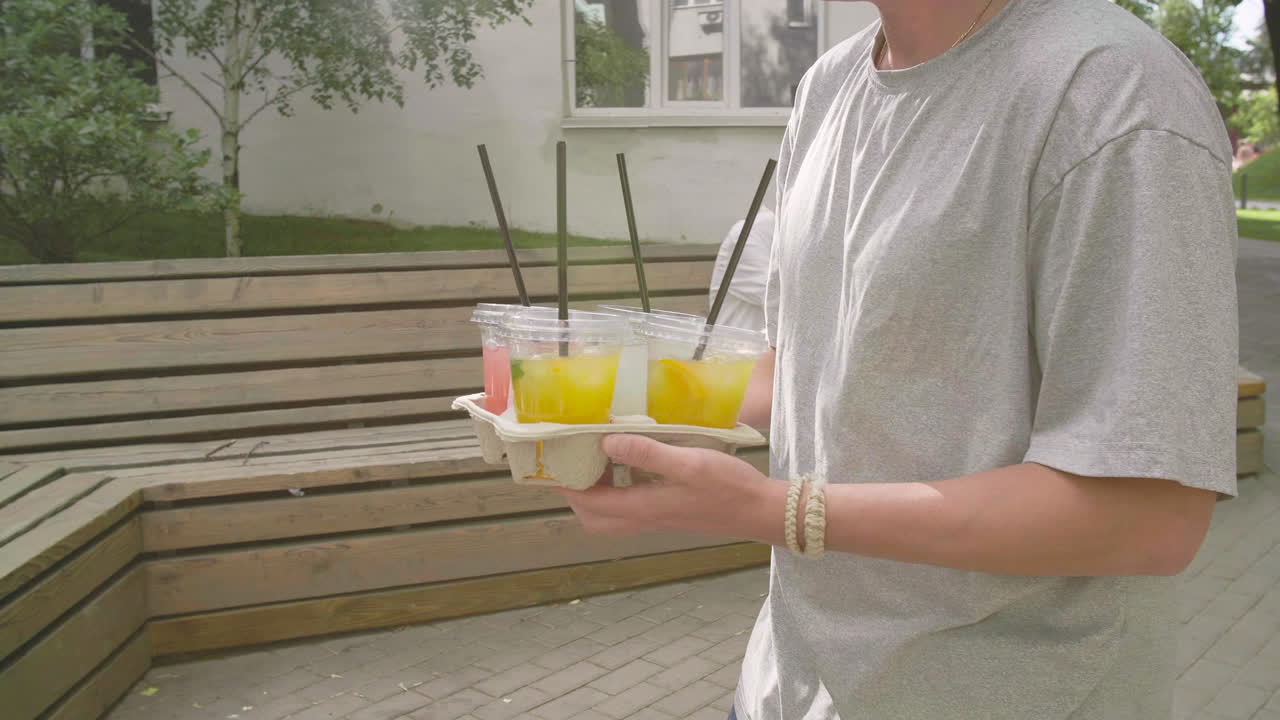 joven diseñador masculino en anteojos en el taller mide piezas de ropa en el estudio y sonríe a la cámara