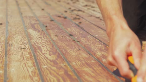 hands using scraper to remove residual mastic weather proof sealant between planking of timber cabin roof