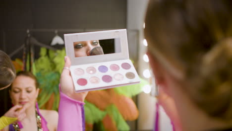 close up of pretty dancer using make up for the show while her colleagues are getting ready in front of her