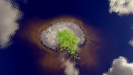 ascending drone video of a very small rock island at the center of a finnish lake in the wilderness