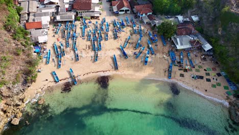 aerial view of a coastal fishing village with numerous blue boats on the beach