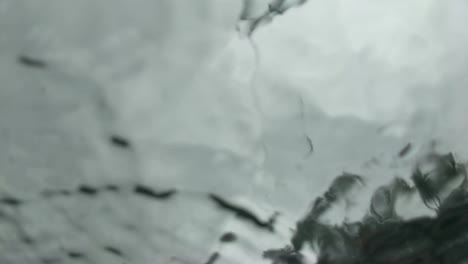 slow motion abstract view of rain drops landing on glass as seen from below, underneath, gray sky