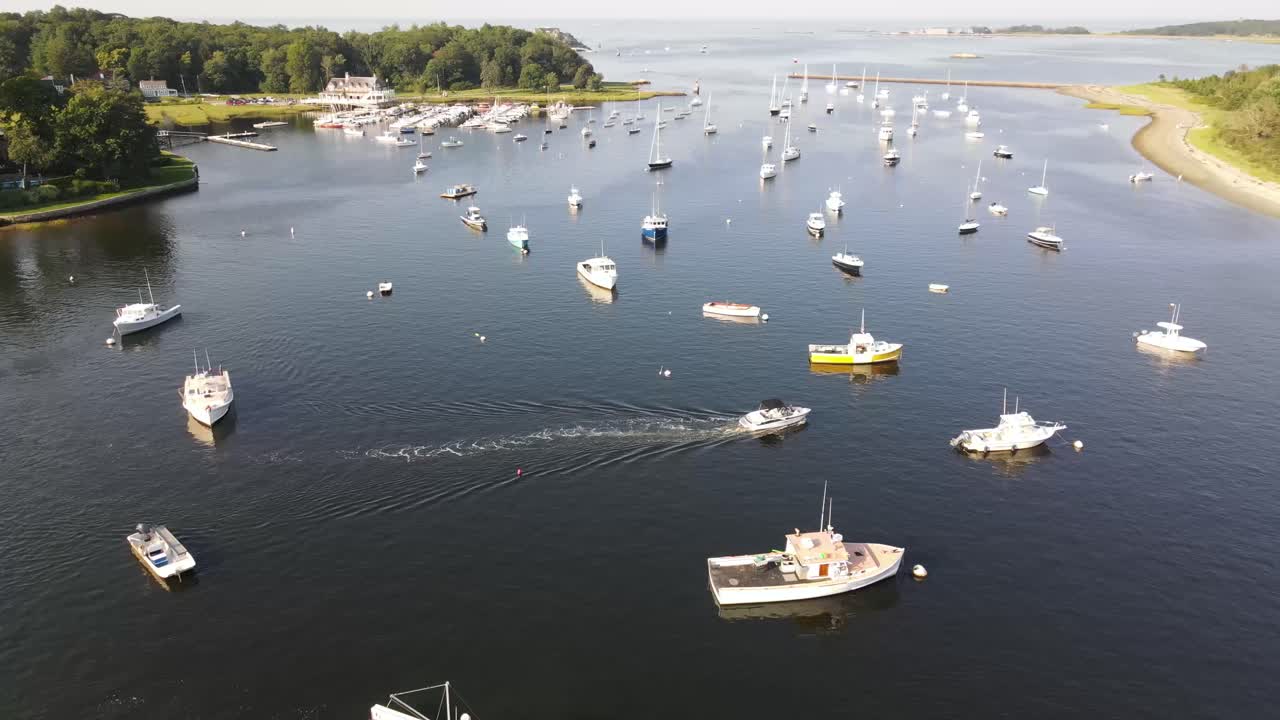Liten båt seiler ved Cohasset Harbor, Massachusetts, med mange båter fortøyd på vannoverflaten