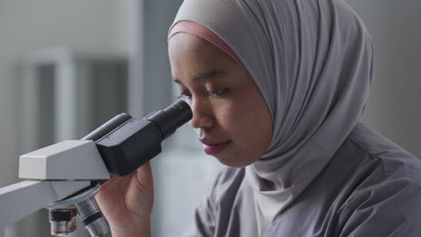 female scientist in hijab conducting research with microscope in laboratory