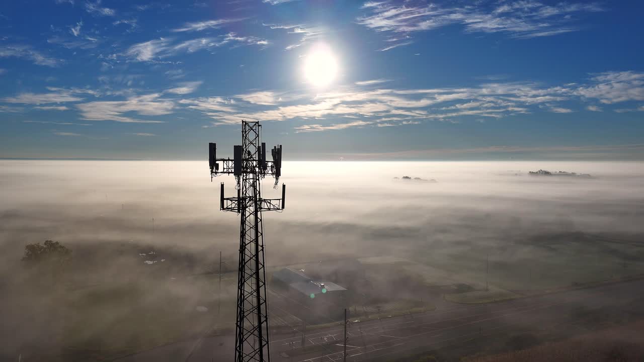 Torre di comunicazione che si erge sopra uno strato di nebbia, garantendo la connettività sotto un cielo azzurro e un sole splendente