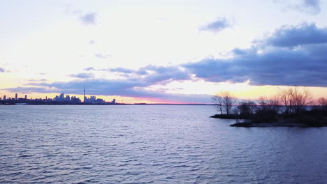 Aerial-flying-over-the-water-with-a-view-of-the-beautiful-Toronto-skyline-at-sunrise